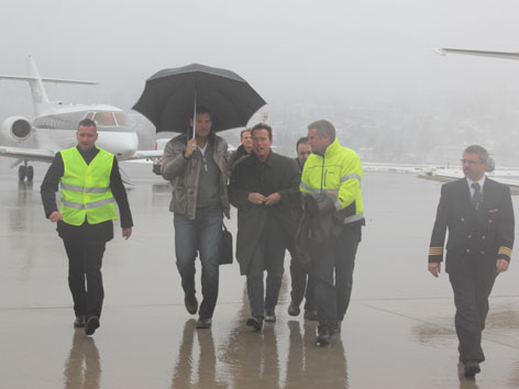Arnold Schwarzenegger mit Ralf Möller und anderen bei starkem Regen am Innsbrucker Flughafen.