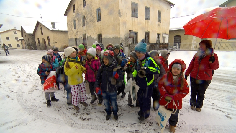 Kinder rufen, läuten ihre Kuhglocken und springen in die Luft, stehen im Dorf im Schnee