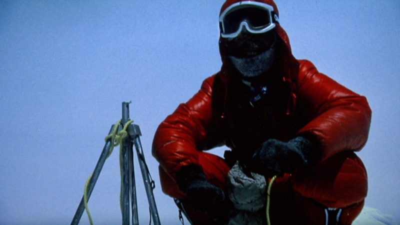 Reinhold Messner ohne Sauerstoff am Gipfel des Mount Everest, in rotem Skianzug und Gesichtsmaske fast nicht zu erkennen